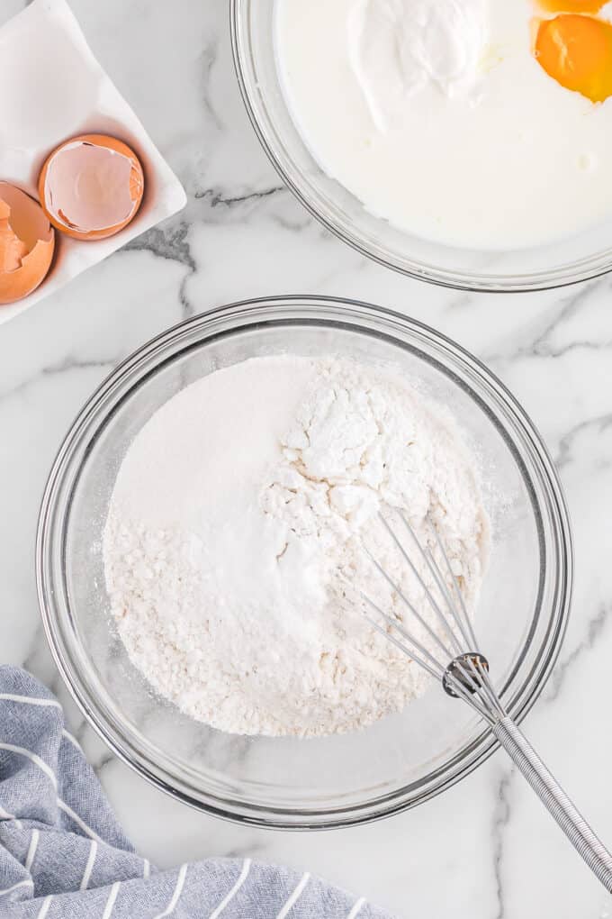 a large glass bowl of flour with a whisk.