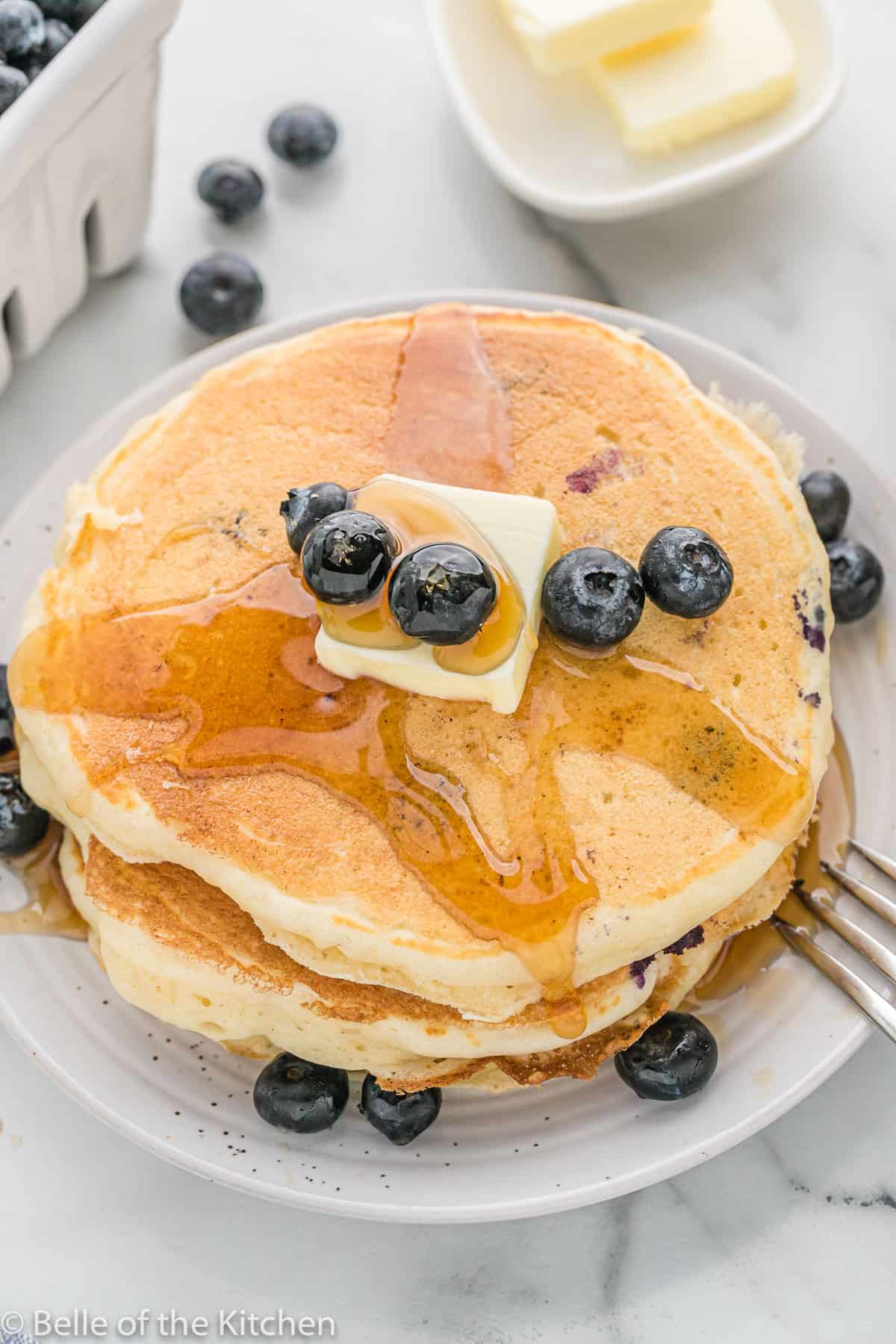 blueberry pancakes on a white plate with butter and syrup.
