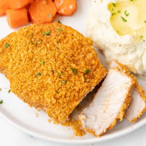 a sliced breaded pork chop on a plate with carrots and mashed potatoes.