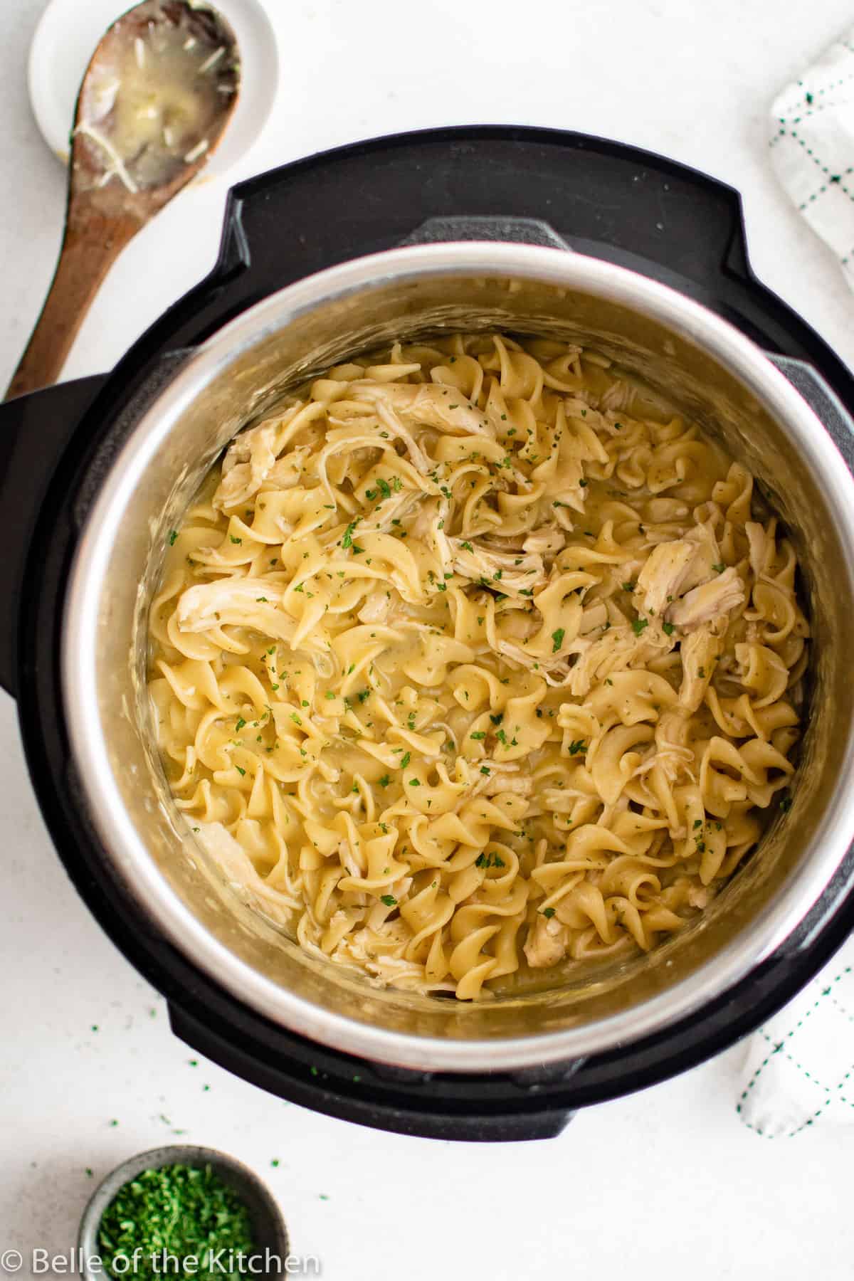 an Instant Pot full of chicken and noodles next to wooden spoon.