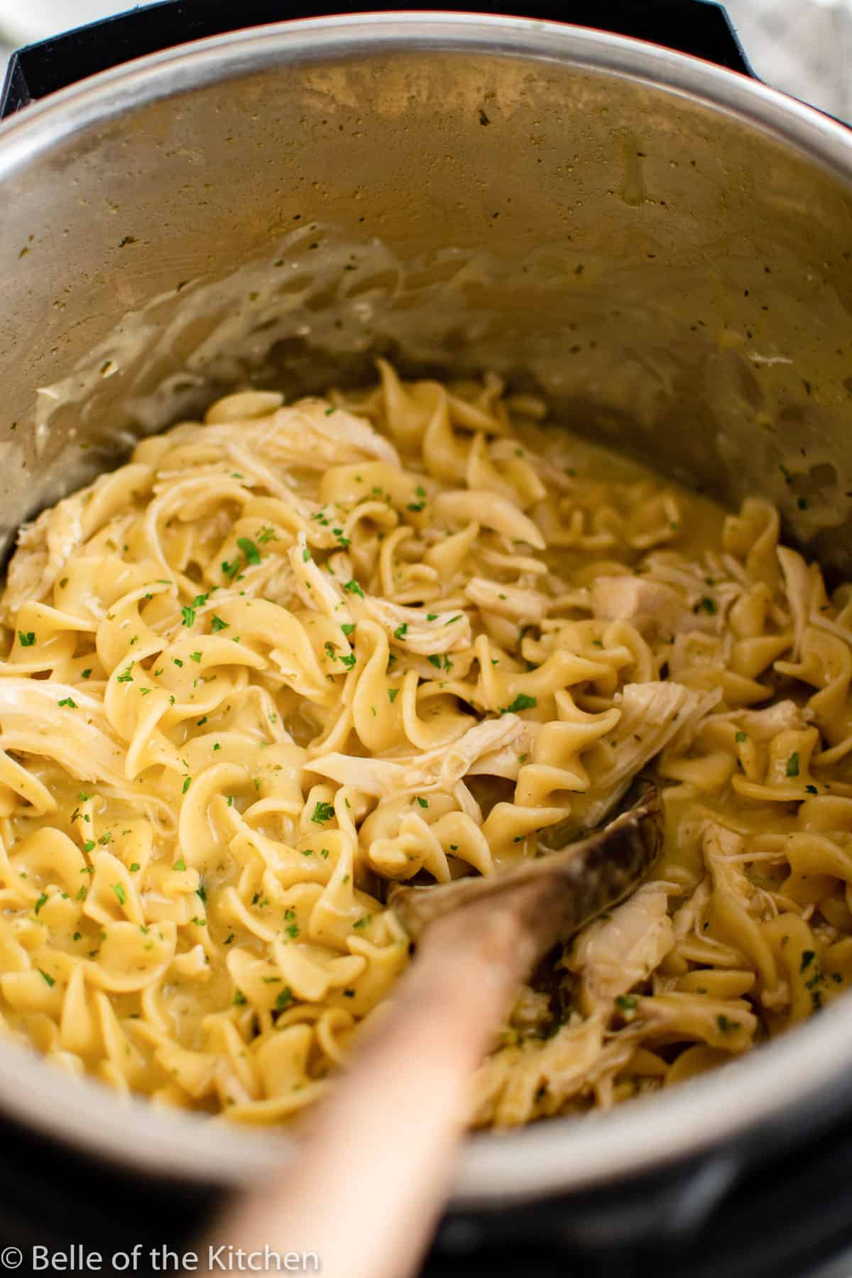 an Instant Pot full of chicken and noodles with a wooden spoon.