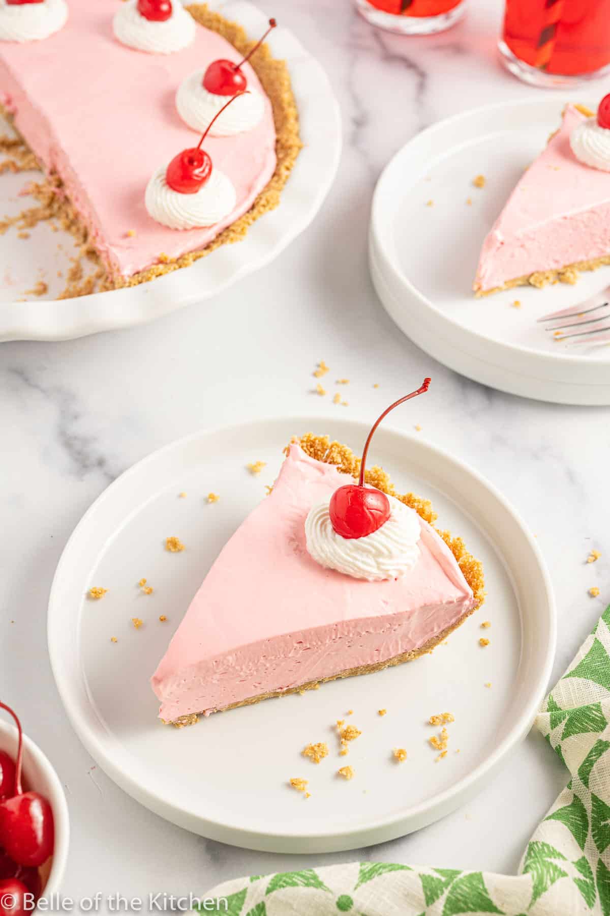 a slice of pink Kool Aid pie on a white plate with a cherry on top.