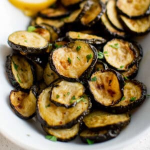 a white bowl of roasted zucchini slices.