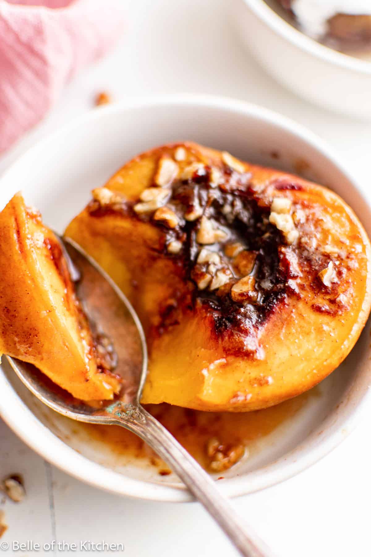 a roasted peach in a white bowl being scooped out with a spoon.