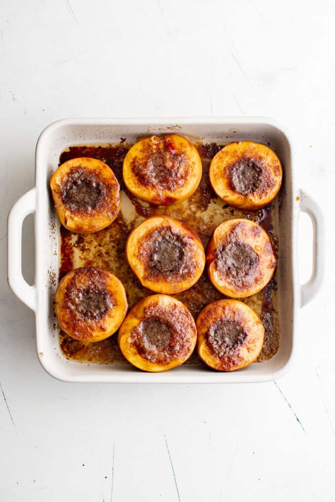 a square baking dish holding roasted peach halves.