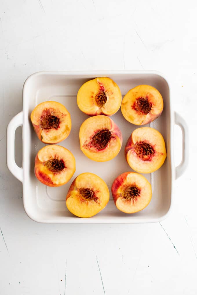 a white square baking dish holding halves peaches.