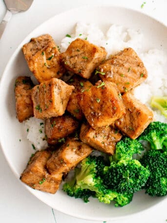 a white plate of rice and cooked salmon bites and broccoli.