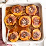 a white baking dish full of roasted peach halves.