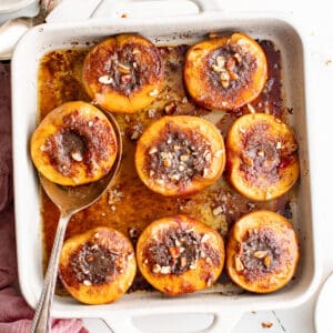 a white baking dish full of roasted peach halves.