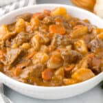 a white bowl filled with beef stew including carrots, beef, and gravy.