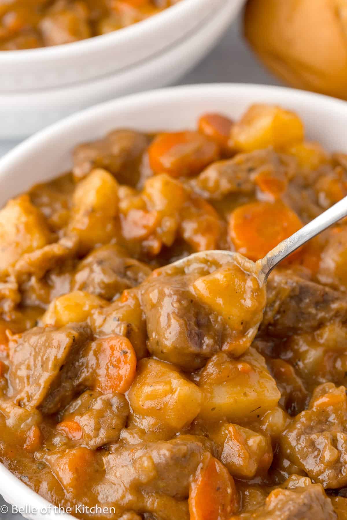 a spoon scooping up beef and potatoes in a white bowl.