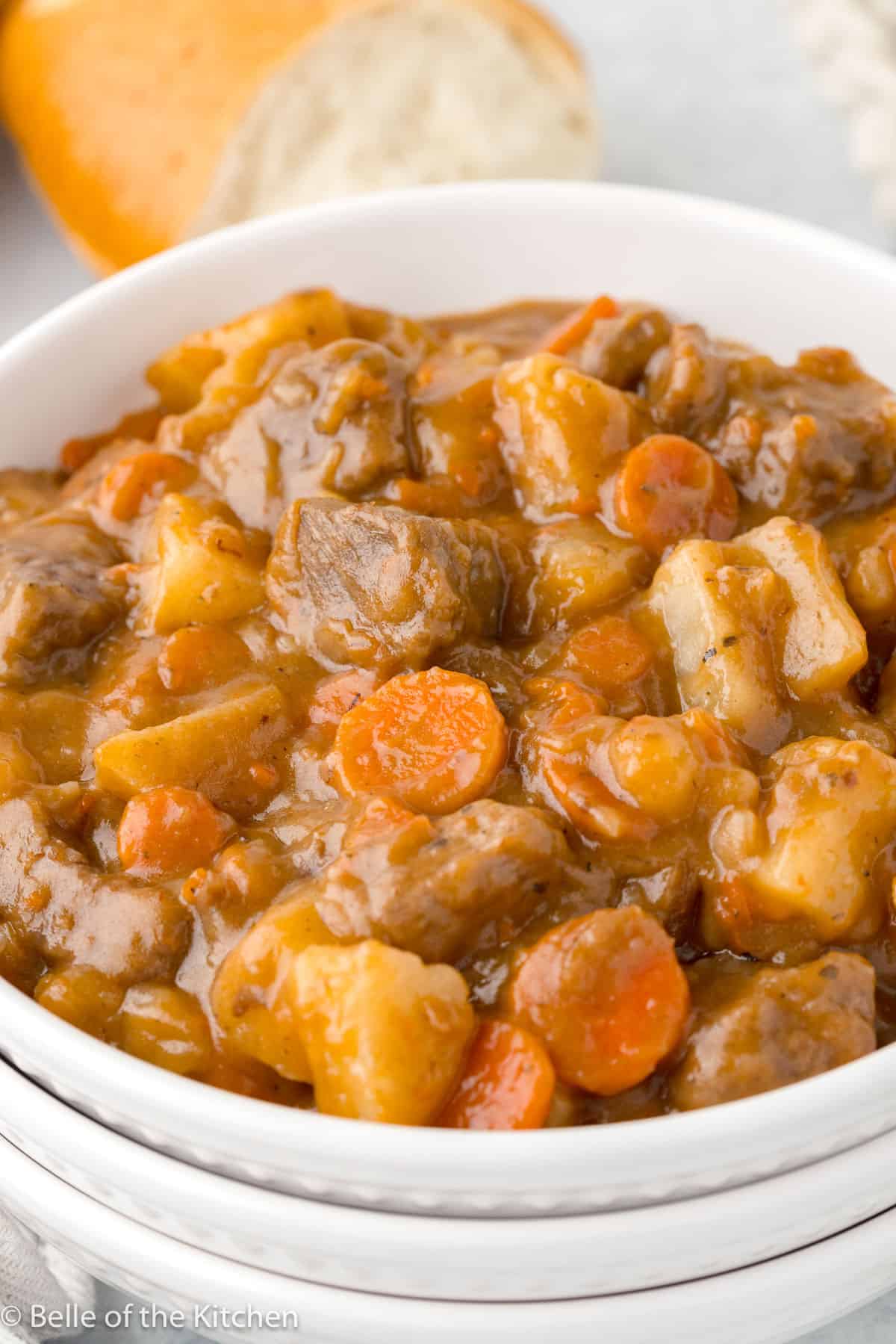 a white bowl filled with beef stew including carrots, beef, and gravy.