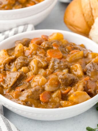 a white bowl filled with beef stew including carrots, beef, and gravy.