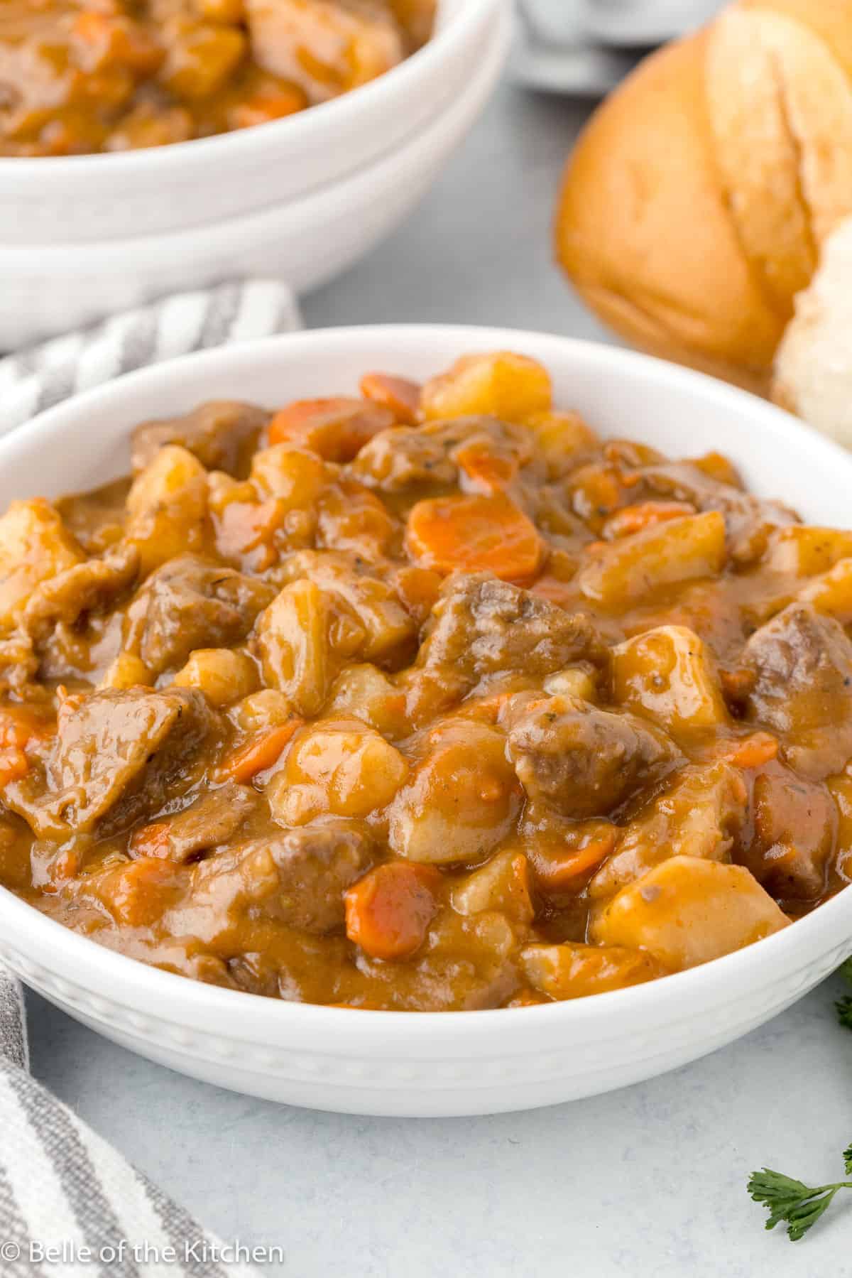 a white bowl filled with beef stew including carrots, beef, and gravy.