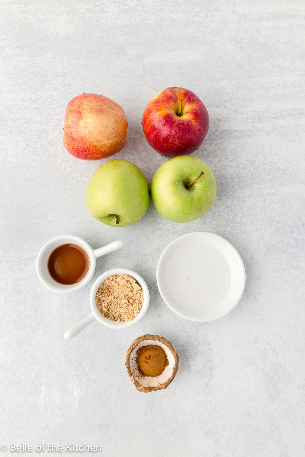 apples next to bowls of cinnamon, brown sugar, and coconut oil on a counter top.