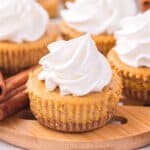 mini pumpkin cheesecakes with whipped cream on top of a wooden board.