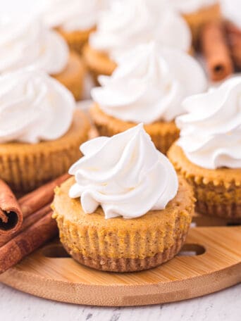 mini pumpkin cheesecakes with whipped cream on top of a wooden board.