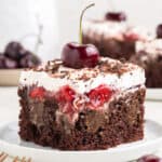 a slice of chocolate cake on a white plate topped with cherries and whipped cream.