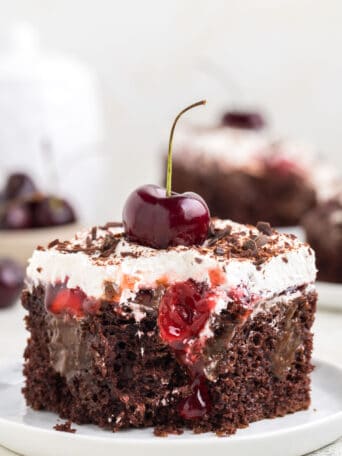 a slice of chocolate cake on a white plate topped with cherries and whipped cream.