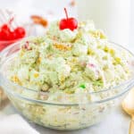 pistachio fluff salad in a glass bowl with a cherry on top.