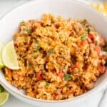 a bowl of cheesy taco rice with a lime wedge on the side.