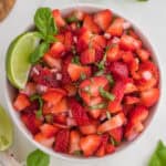 a bowl of chopped strawberries with basil and limes.