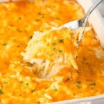 a spoon scooping hashbrown casserole from a white baking dish.