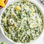 a white bowl full of spinach and artichoke dip.