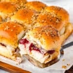 a metal spoon holding a turkey slider sandwich with cranberry sauce.