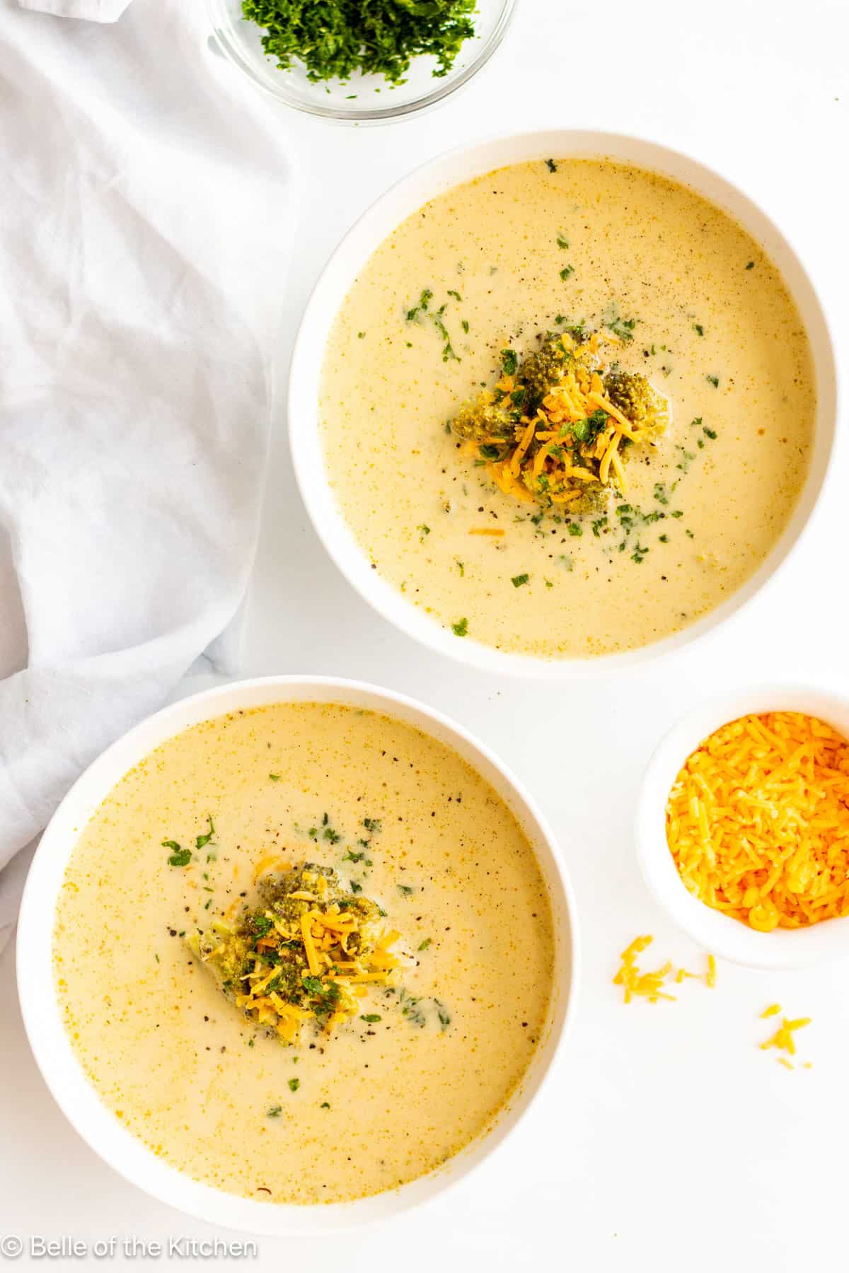 Two white bowls full of broccoli cheddar soup.