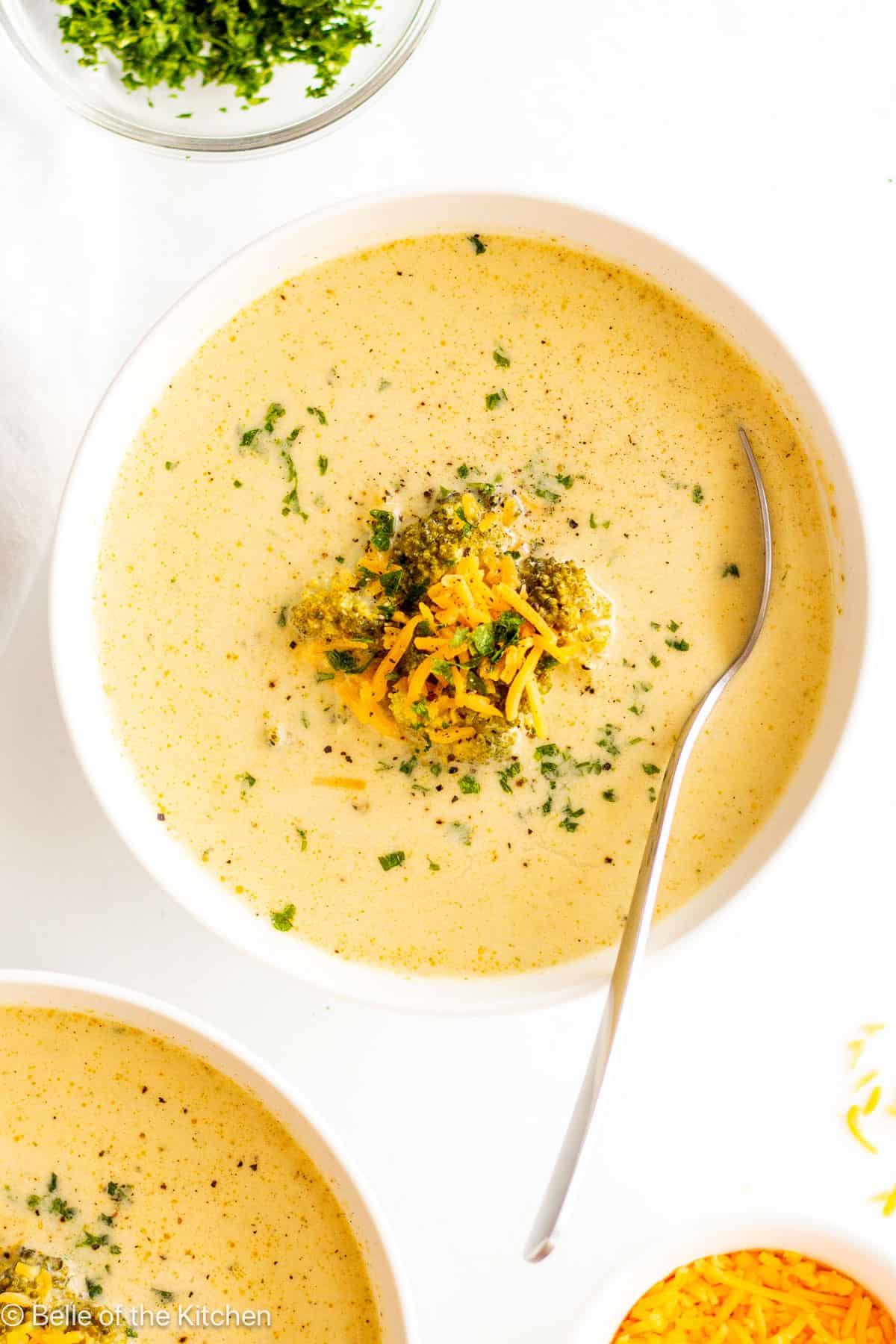 A white bowl full of broccoli cheddar soup with a spoon.