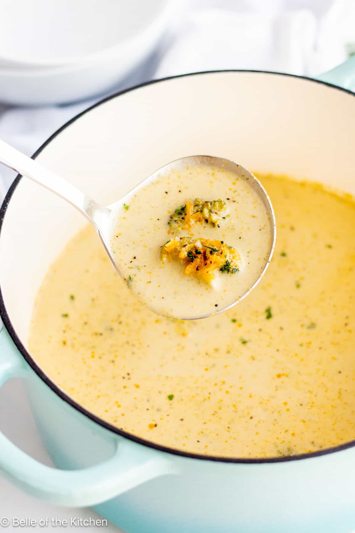 A dutch oven full of broccoli cheddar soup with a ladle scooping some out.