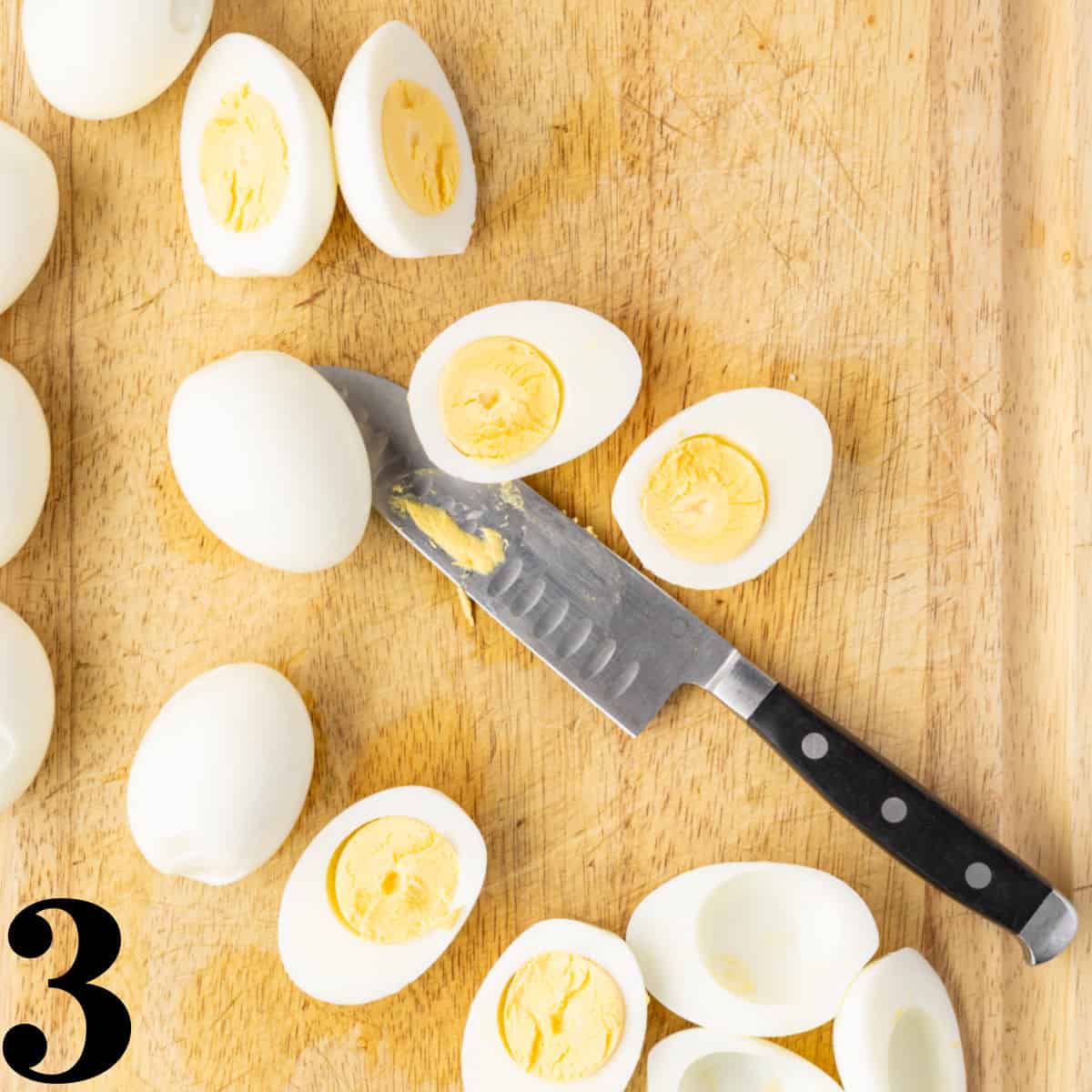 a wooden cutting board with a knife and hard boiled eggs cut in half.