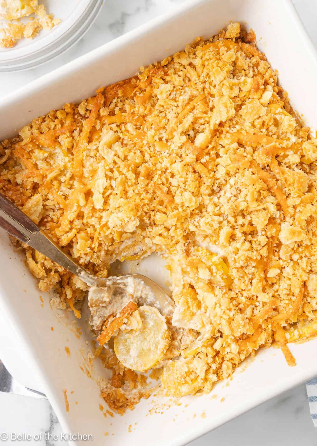 A spoon scooping up squash casserole from a baking dish.