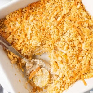 A spoon scooping up squash casserole from a baking dish.