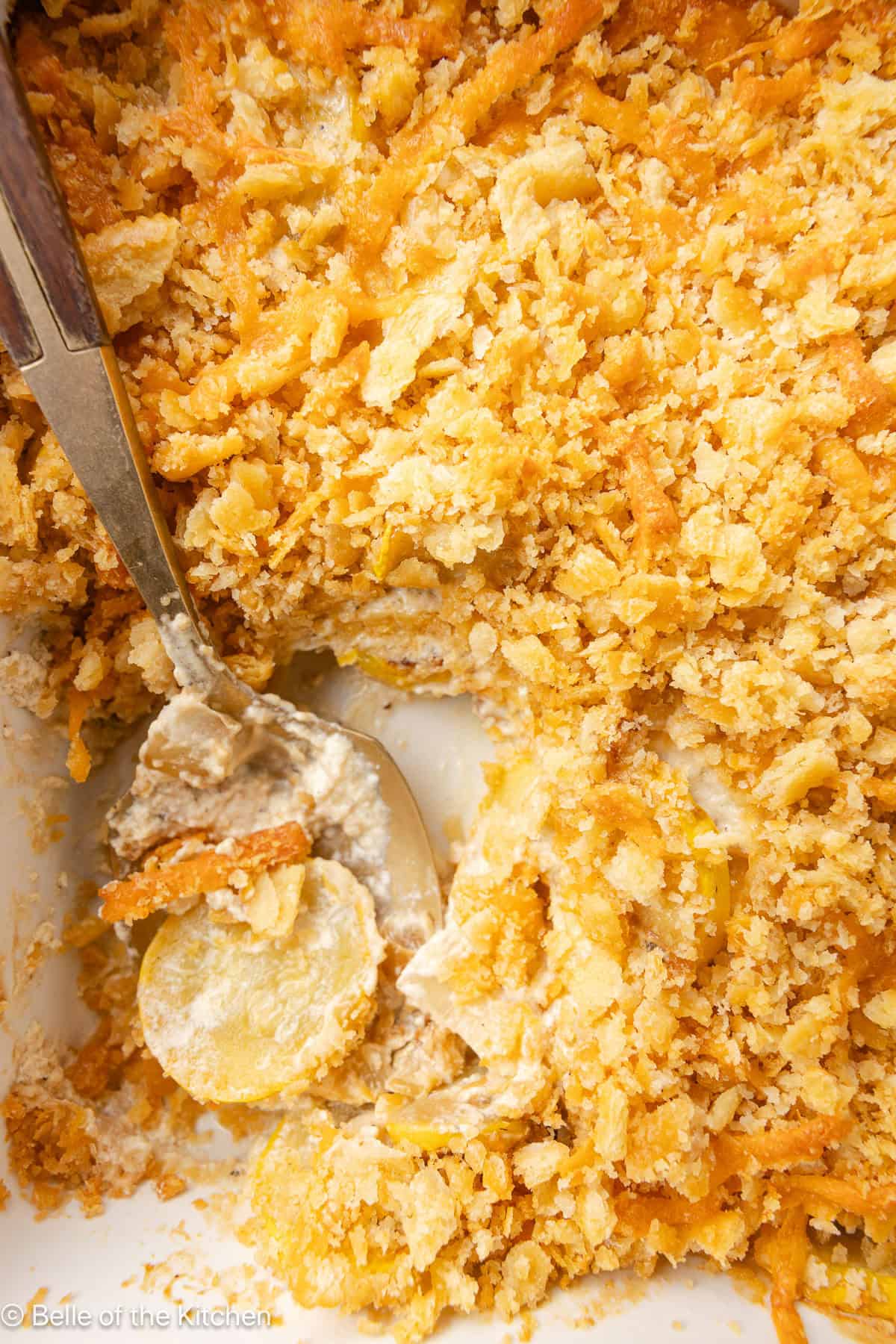 A spoon scooping up squash casserole from a baking dish.