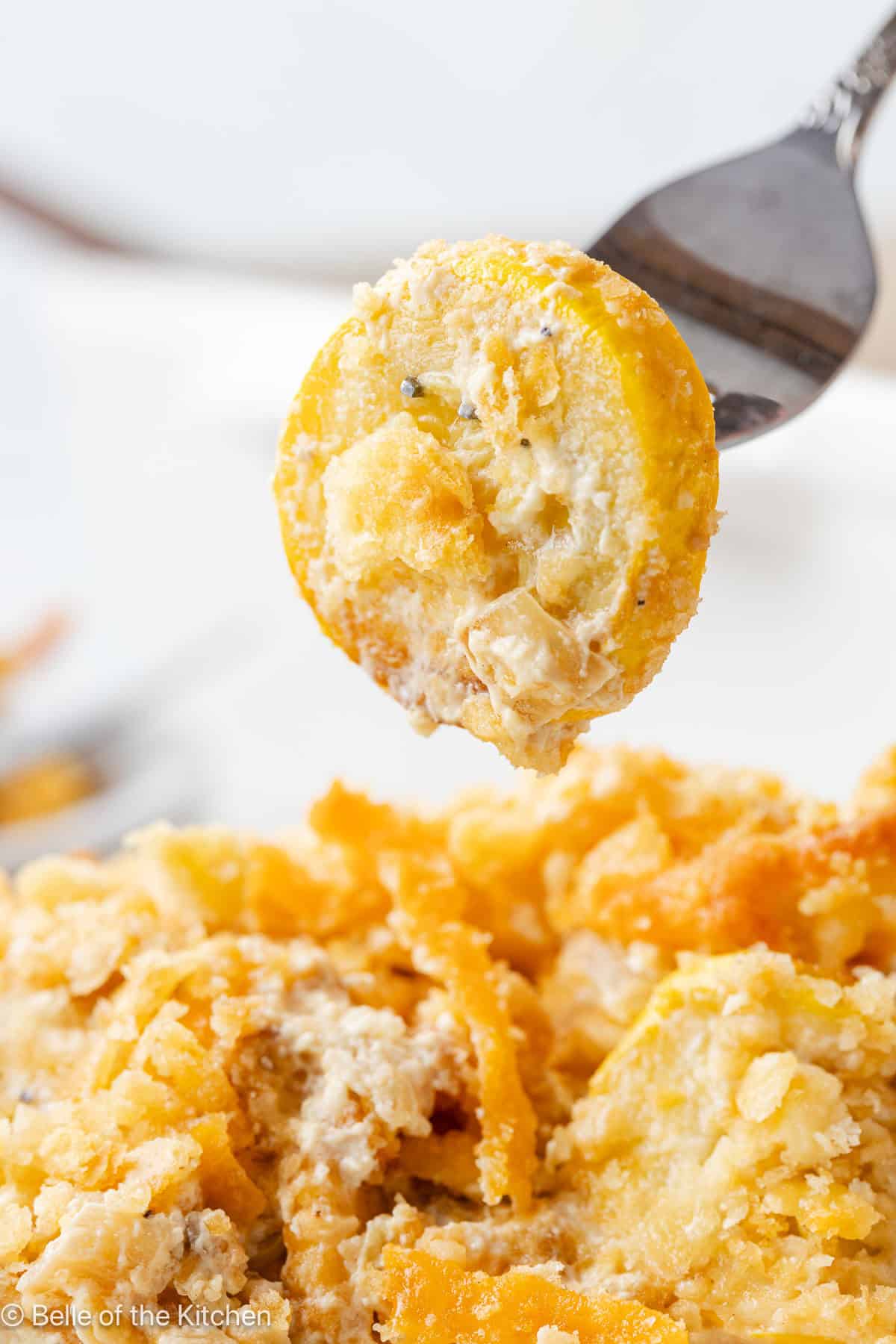 A fork scooping up a piece of yellow squash from a casserole.