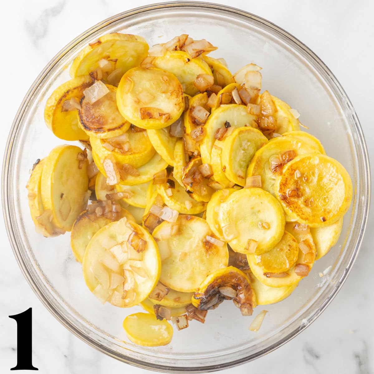 A glass bowl of sliced squash with onions.