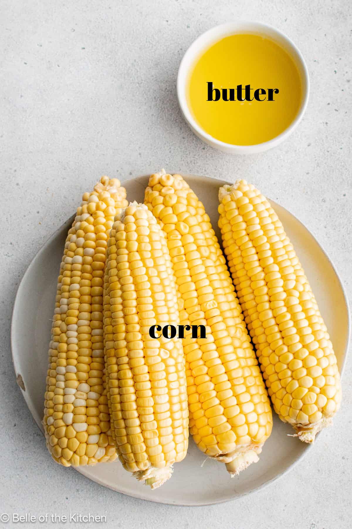 corn on a plate next to a bowl of melted butter.