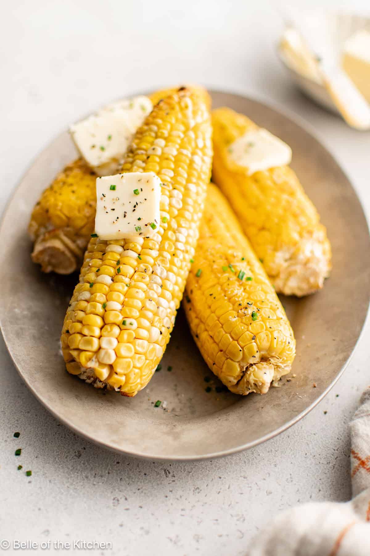 Ears of cooked corn on a plate with pats of butter on top.