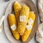 Ears of cooked corn on a plate with pats of butter on top.