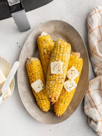 Ears of cooked corn on a plate with pats of butter on top.