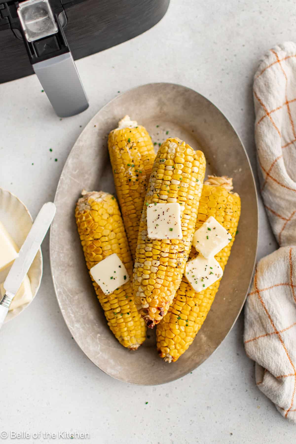 Ears of cooked corn on a plate with pats of butter on top.