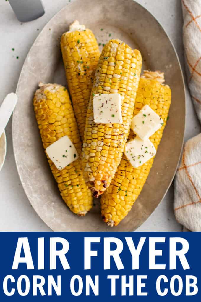 Ears of cooked corn on a plate with pats of butter on top.