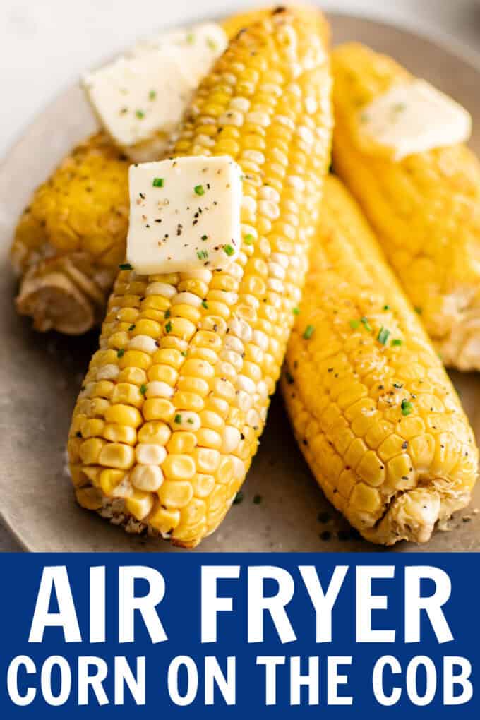 Ears of cooked corn on a plate with pats of butter on top.