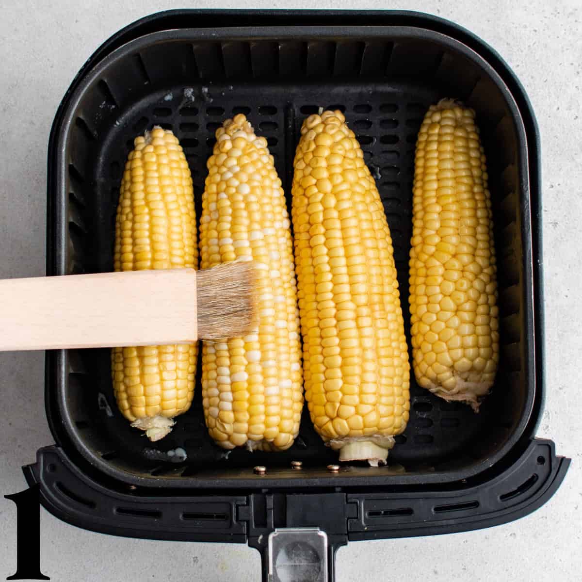 Ears of corn in an air fryer basket.