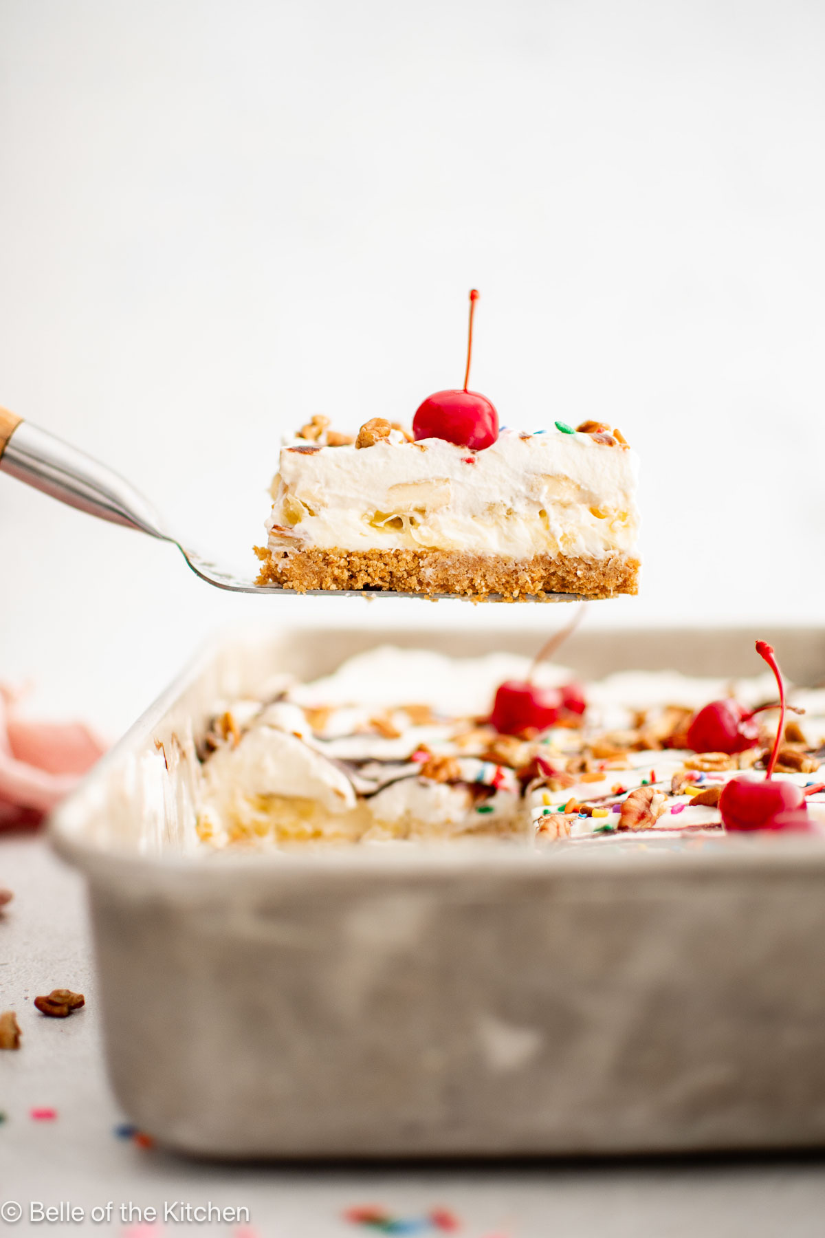 A slice of banana split cake being lifted out of a pan.