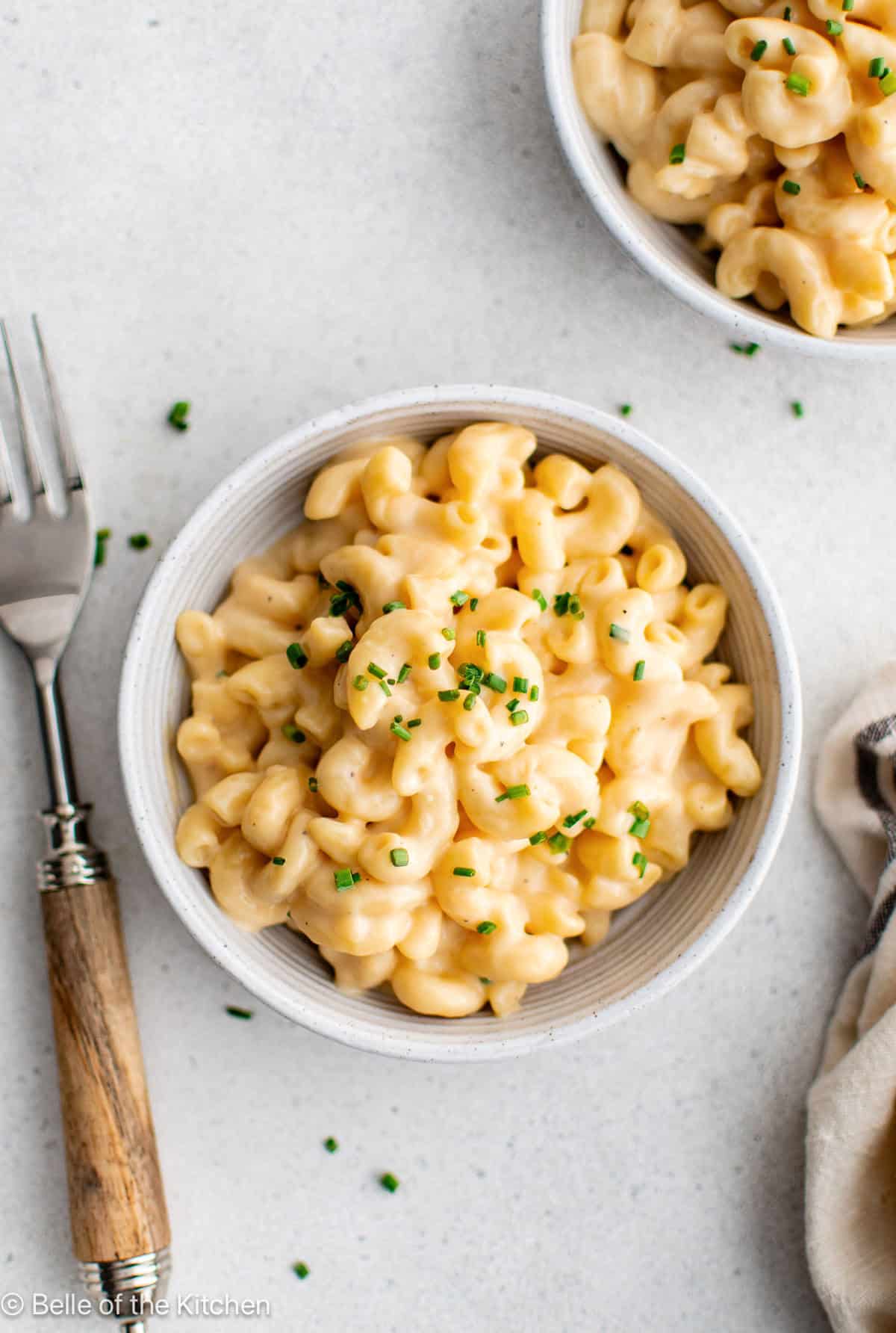 A white bowl of macaroni and cheese next to a fork.