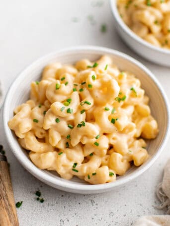A white bowl of macaroni and cheese next to a fork.