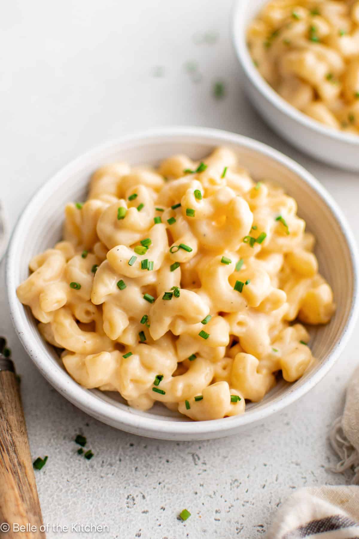 A white bowl of macaroni and cheese next to a fork.